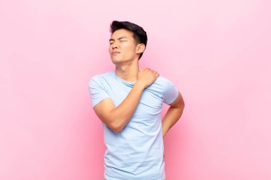 Genç Çinli bir adam yorgun, stresli, endişeli, hayal kırıklığına uğramış ve depresif hissediyor. Sırtı ya da boynu düz duvarda ağrıyor.