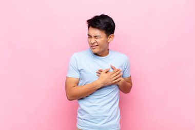 Genç Çinli adam üzgün, yaralı ve kalbi kırık görünüyor. İki elini de kalbe yakın tutuyor. Ağlıyor ve depresif hissediyor.