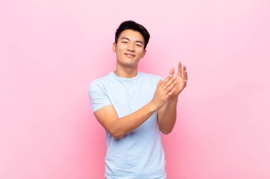 Genç Çinli adam kendini mutlu ve başarılı hissediyor, gülümseyen ve alkışlayan eller, düz renkli duvara karşı alkış ile tebrik ediyor.