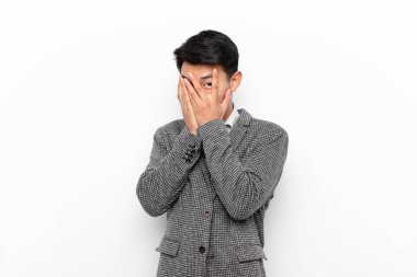 Genç Çinli bir adam korkmuş ya da utanmış hisseder. Gözleri yarı çıplak bir şekilde duvara bakar ya da gözetler.