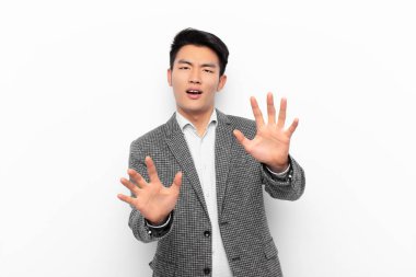 Genç Çinli adam korku ve panik içinde geri çekilip çığlık atıyor. Düz renkli duvara karşı bir kabusa tepki veriyor.