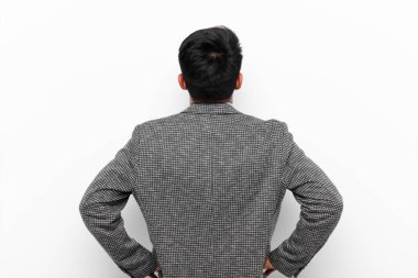 Genç Çinli adamın kafası karışık ya da dolu ya da şüphe ve soru dolu, merak ediyorum, elleri kalçasında, düz renkli duvara karşı dikiz manzaralı