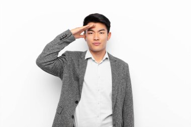 Genç Çinli bir adam kameraya askeri bir selamlama ile selam veriyor onur ve vatanseverlik göstergesi olarak, düz renk duvarına karşı saygı gösteriyor.