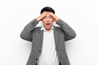 Genç Çinli adam dehşete kapılmış ve şok olmuş hissediyor. Düz renkli duvara karşı yapılan bir hatadan dolayı el ele tutuşup panikliyor.