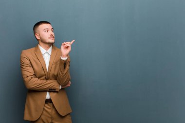 Genç yakışıklı işadamı mutlu bir şekilde gülümsüyor ve yan bakıyor, merak ediyor, düşünüyor ya da düz arkaplana karşı bir fikir üretiyor.