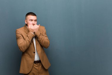 Genç yakışıklı adam endişeli, endişeli, stresli ve korkmuş görünüyor. Tırnaklarını yiyor ve düz arkaplana karşı yanal fotokopi çekmeye çalışıyor.