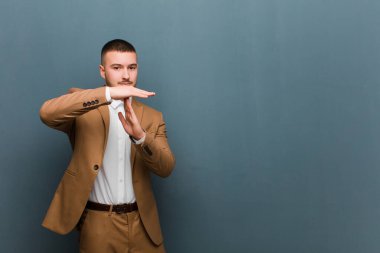 Genç yakışıklı adam ciddi, sert, kızgın ve hoşnutsuz görünüyor. Düz arkaplanda mola işareti yapıyor.