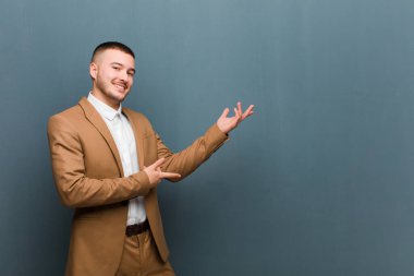 Genç yakışıklı adam gururla ve güvenle gülümsüyor, mutlu ve tatmin olmuş hissediyor ve düz arkaplana karşı fotokopi alanında bir konsept gösteriyor.