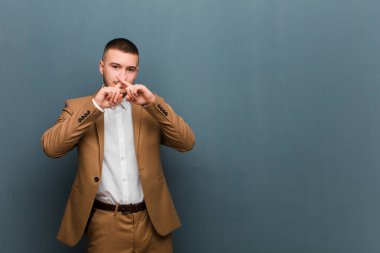 Genç ve yakışıklı bir adam ciddi görünüyor ve iki parmağının önde olması hoşnutsuzca reddedilerek düz arkaplan karşısında sessizlik istiyor.