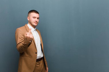 Genç ve yakışıklı bir adam kızgın, sinirli, asi ve agresif orta parmağını sallayarak düz arkaplana karşı savaşıyor.