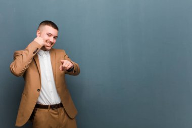 Genç ve yakışıklı bir adam neşeyle gülümsüyor ve kamerayı işaret ediyor. Daha sonra seni telefonla ararken düz arkaplan karşısında konuşuyor.