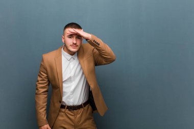 Genç yakışıklı adam şaşkın ve şaşkın görünüyor, el üstünde uzak bakıyor, düz arkaplan karşı izlemek ya da arama