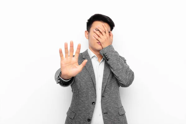 若い中国人男性が手で顔をカバーし フラットカラーの壁に対して写真や写真を拒否し カメラを停止するために前に手を置く — ストック写真