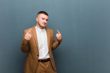 Kötü tavırlı genç yakışıklı işadamı gururlu ve agresif görünüyor, yukarı bakıyor ya da düz arkaplan üzerinde ellerle dalga geçiyor.