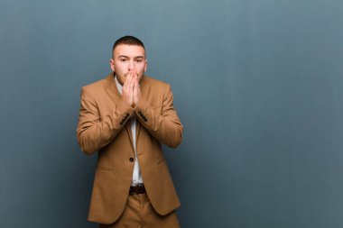 Genç yakışıklı iş adamı endişeli, üzgün ve korkmuş hissediyor, elleriyle ağzını kapatıyor, endişeli görünüyor ve düz arkaplana karşı işleri berbat ediyor.