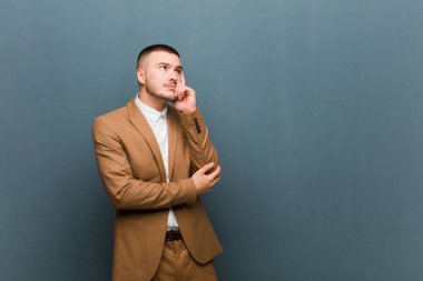 Genç yakışıklı iş adamı, konsantre bir bakışla, şüpheli bir ifadeyle merak, düz arkaplan karşısında yukarı ve yana bakıyor