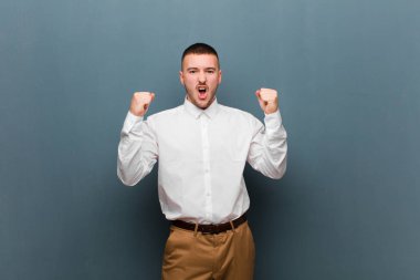 Genç yakışıklı iş adamı sinirli bir ifadeyle ya da düz arkaplana karşı başarıyı kutlayan yumruklarla agresif bir şekilde bağırıyor.