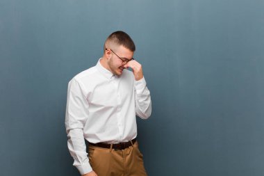 Genç yakışıklı iş adamı stresli, mutsuz ve hayal kırıklığına uğramış, alnına dokunmuş ve şiddetli baş ağrısı çeken düz fon.