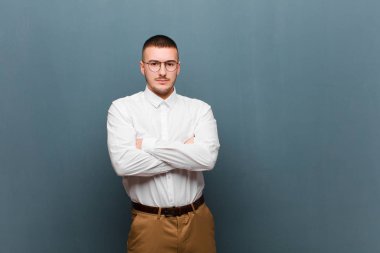 Genç ve yakışıklı iş adamı hayal kırıklığına uğramış ve hayal kırıklığına uğramış hissediyor, ciddi görünüyor, sinirli ve kollarını düz arkaplana karşı çaprazlamış.