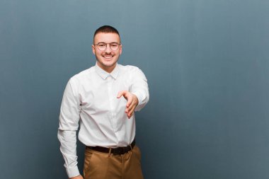 Genç yakışıklı iş adamı gülümsüyor, mutlu, kendinden emin ve arkadaş canlısı görünüyor, anlaşmayı bitirmek için el sıkışma teklif ediyor, düz arkaplan karşısında işbirliği yapıyor.