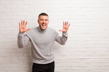 Genç ve yakışıklı bir adam panik ya da öfke içinde bağırıyor, şok olmuş, korkmuş ya da öfkeli, elleri düz duvara dayalı.