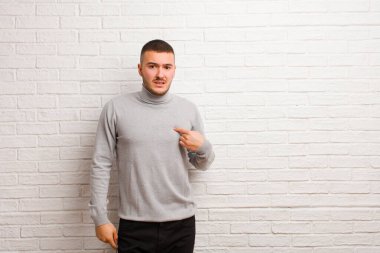 Kafası karışmış, kafası karışmış ve kendine güveni olmayan genç yakışıklı bir adam kendini gösterip kim olduğumu soruyor, ben mi? yassı duvara karşı