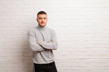Genç, yakışıklı bir adam hayal kırıklığına uğramış, hayal kırıklığına uğramış, ciddi görünüyor, kızgın ve kollarını düz duvara dayamış.