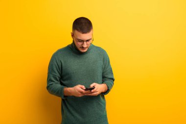 Akıllı telefonlu, düz duvara yaslanmış genç yakışıklı adam.