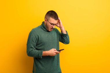 Akıllı telefonlu, düz duvara yaslanmış genç yakışıklı adam.