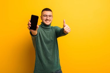 Akıllı telefonlu, düz duvara yaslanmış genç yakışıklı adam.