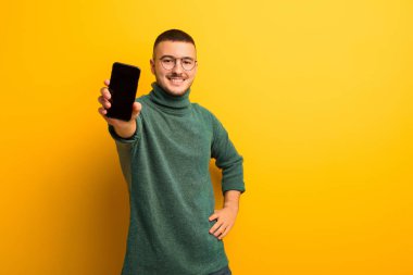 Akıllı telefonlu, düz duvara yaslanmış genç yakışıklı adam.