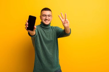 Akıllı telefonlu, düz duvara yaslanmış genç yakışıklı adam.