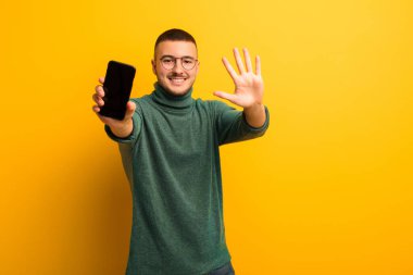 Akıllı telefonlu, düz duvara yaslanmış genç yakışıklı adam.