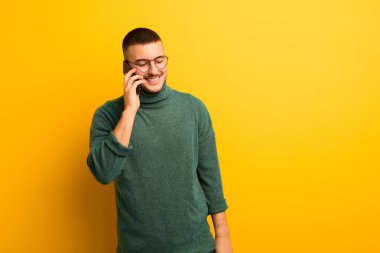 Akıllı telefonlu, düz duvara yaslanmış genç yakışıklı adam.