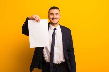 Genç ve yakışıklı bir iş adamı arka planda boş bir kağıt parçası tutuyor.