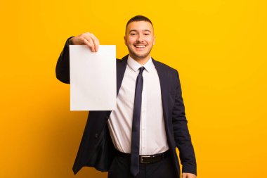 Genç ve yakışıklı bir iş adamı arka planda boş bir kağıt parçası tutuyor.