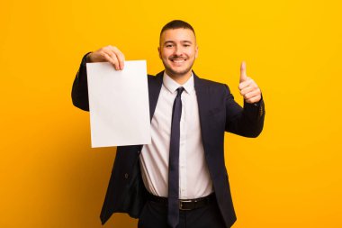 Genç ve yakışıklı bir iş adamı arka planda boş bir kağıt parçası tutuyor.