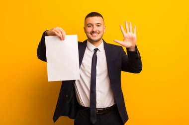 Genç ve yakışıklı bir iş adamı arka planda boş bir kağıt parçası tutuyor.