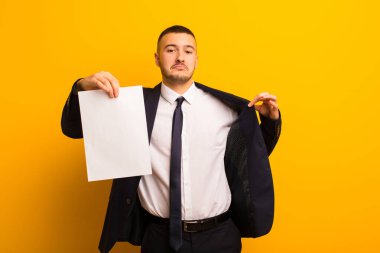 Genç ve yakışıklı bir iş adamı arka planda boş bir kağıt parçası tutuyor.