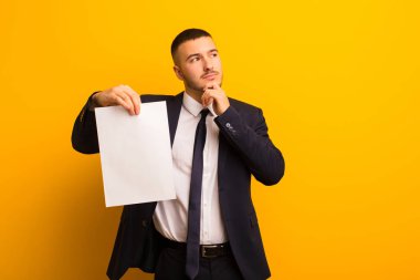 Genç ve yakışıklı bir iş adamı arka planda boş bir kağıt parçası tutuyor.