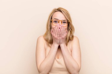 Genç ve güzel sarışın kadın mutlu, neşeli, şanslı ve şaşırmış görünüyor. İki eli de düz duvarda.