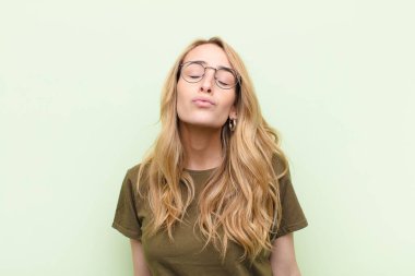 Genç, güzel sarışın kadın dudaklarını birbirine bastırıyor. Sevimli, eğlenceli, mutlu, sevimli bir yüz ifadesiyle. Düz renkli duvara bir öpücük yolluyor.