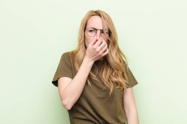Genç, güzel sarışın kadın iğreniyor. Düz renkli duvardaki pis ve tatsız kokuyu koklamamak için burnunu tutuyor.