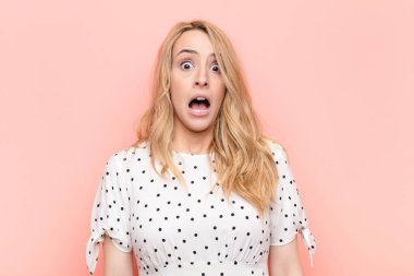 Genç, güzel sarışın kadın şok olmuş ya da şaşırmış görünüyor, ağzı açık bir şekilde düz duvara karşı 