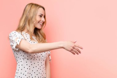 Genç, güzel sarışın kadın gülümsüyor, seni selamlıyor ve başarılı bir anlaşma için el sıkışmayı teklif ediyor.