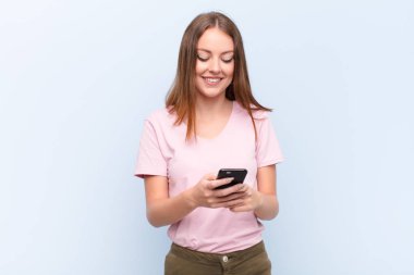 Genç kızıl saçlı kadın düz duvara karşı akıllı telefonuyla