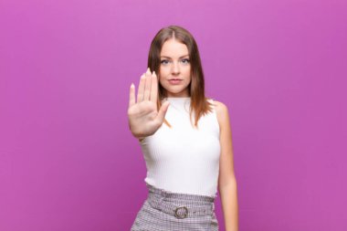 Genç kızıl saçlı kadın ciddi, sert, hoşnutsuz ve kızgın görünüyor. Avuç içini açıp düz duvara karşı jest yapıyor.