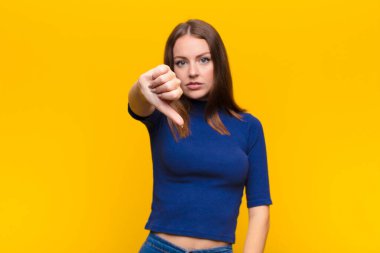 Genç kızıl saçlı kadın kızgın, sinirli, hayal kırıklığına uğramış ya da hoşnutsuz, düz duvara karşı ciddi bir bakışla başparmağını kaldırıyor.