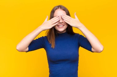 Genç kızıl saçlı kadın gülümsüyor ve mutlu hissediyor, iki eliyle gözlerini kapatıyor ve düz duvara karşı inanılmaz bir sürpriz bekliyor.