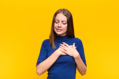 Genç kızıl saçlı kadın üzgün, yaralı ve kalbi kırık görünüyor, iki elini de kalbe yakın tutuyor, ağlıyor ve yassı duvara karşı depresif hissediyor